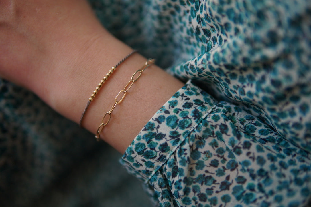 Zierliches 14 kt Goldfilled Armband Marilou am Handgelenk einer Person mit blau-grünem Leopardenmuster-Outfit, feine Goldperlen und elegante Kettenglieder
