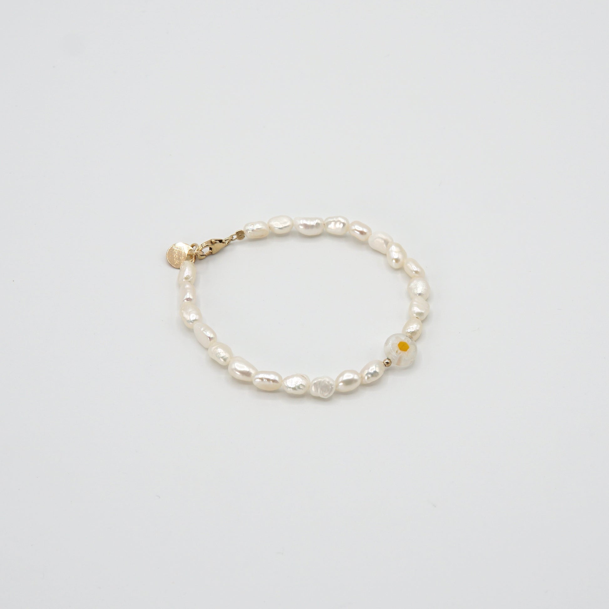 Armband 'WHITE FLOWER' mit schimmernden Süßwasserperlen, Gänseblümchen-Glasperle und goldenen Akzenten, elegant am Handgelenk getragen.
